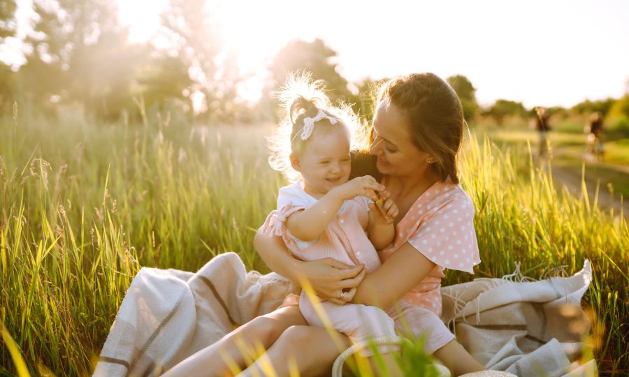 Mother and daughter playing together in summer park at sunset. Happy mom with small child having fun